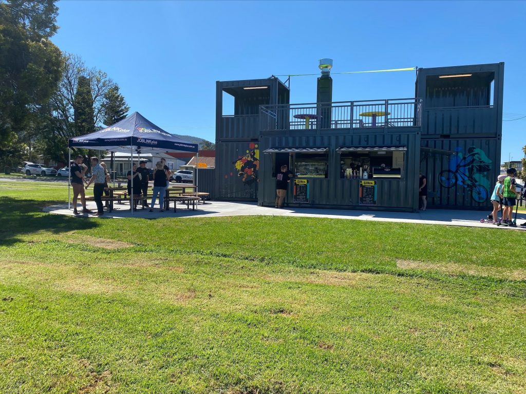 exterior of the cafe showing grassy areas, people gathered, a sunny day